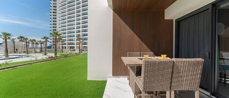 A modern outdoor seating area with a pool view, a tall building in the background, and a clear sky.
