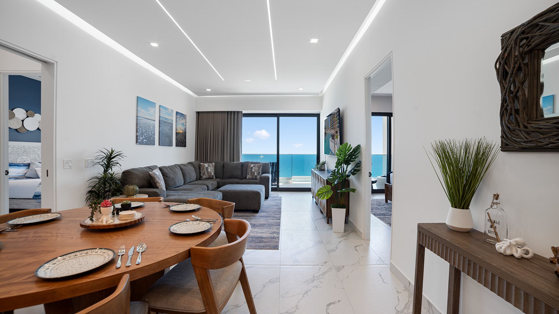 A modern living room with a large window overlooking the sea, a dining area with a wooden table and chairs, and a cozy seating area with a sofa.