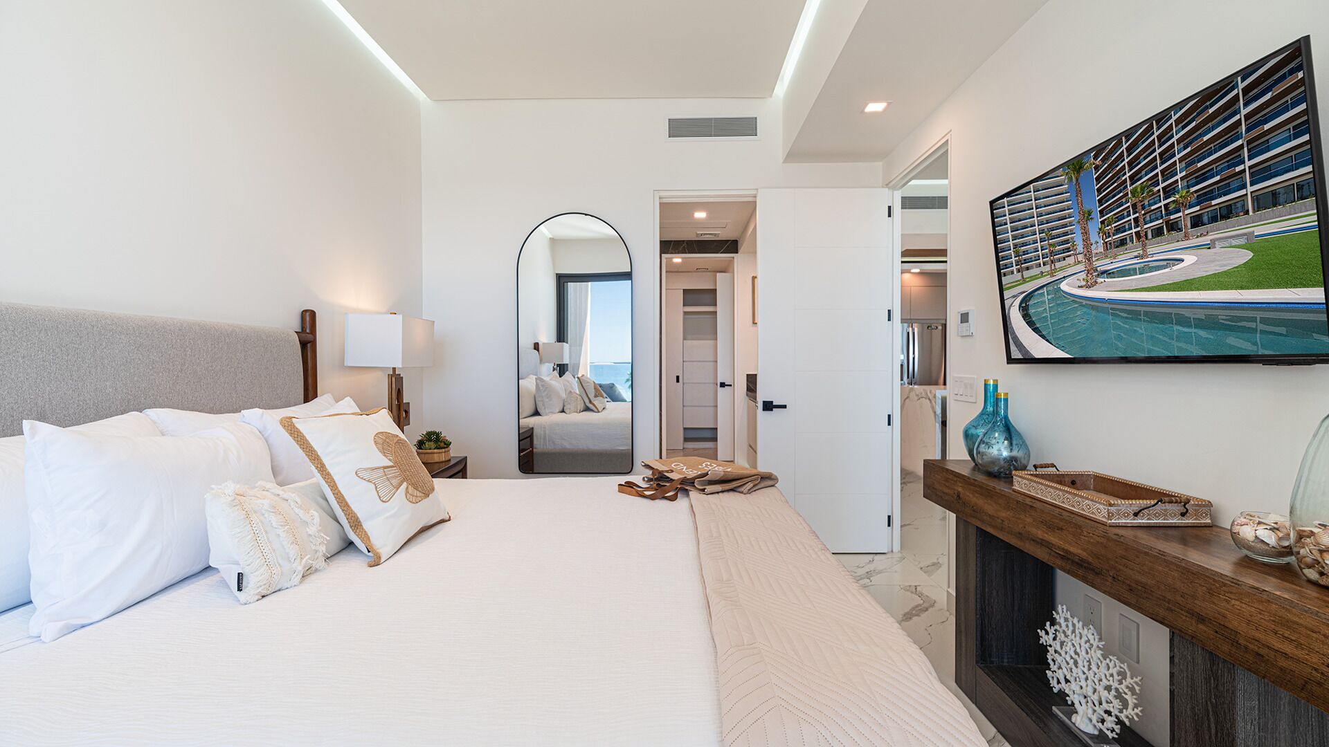Una habitación de hotel moderna con una cama grande, un espejo, un cuadro de una piscina y vista al área de la piscina.