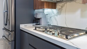A modern kitchen with a stainless steel refrigerator, a built-in oven, and a marble backsplash. - Encantame Soleil (Puerto Peñasco)
