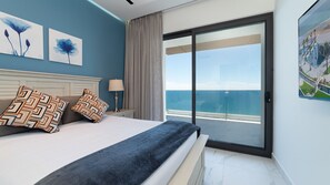 A hotel room with a bed, a nightstand, a lamp, a view of the sea, and two wall art pieces. - Encantame Soleil (Puerto Peñasco)