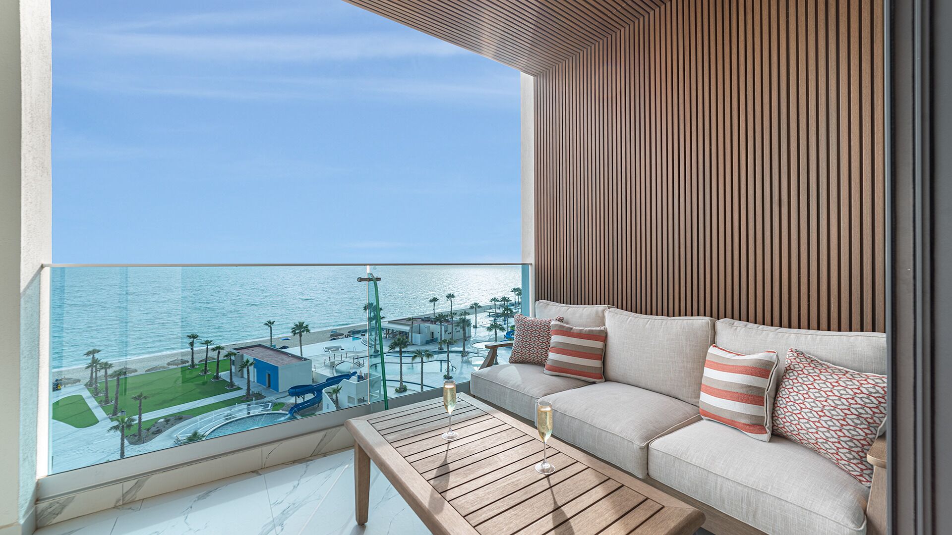 A balcony with a sofa and table, overlooking a pool and beach area.