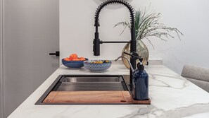 A kitchen with a modern faucet, a sink, and two bowls of fruit on the counter. - Encantame Soleil (Puerto Peñasco)