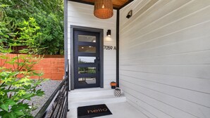 A modern house entrance with a black door, a number plaque, and a wicker light fixture. - Modern Stunner Walkable to Lake Travis + Views! (Austin)