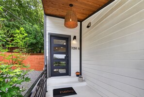 A modern house entrance with a black door, a number plaque, and a wicker light fixture. - Modern Stunner Walkable to Lake Travis + Views! (Austin)