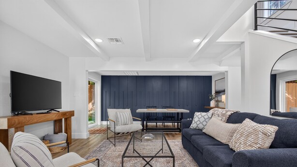 A modern living room with a flat-screen TV, a sofa, a dining table, and a chair. - Modern Stunner Walkable to Lake Travis + Views! (Austin)