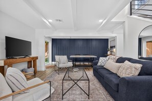A modern living room with a flat-screen TV, a sofa, a dining table, and a chair.