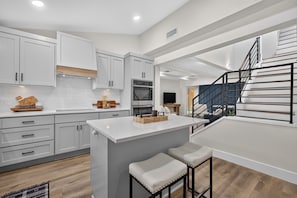 Una cocina moderna con armarios blancos, una isla central y una escalera que sube a un nivel superior.