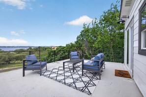A balcony with outdoor furniture, a patterned rug, and a view of the sea. - Modern Stunner Walkable to Lake Travis + Views! (Austin)