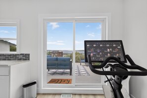 A home gym with a stationary bike, a blue chair, and a view of the outdoors through a sliding door. - Modern Stunner Walkable to Lake Travis + Views! (Austin)