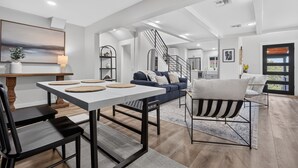 A modern living room with a dining area, a staircase, and a view of the outdoors. - Modern Stunner Walkable to Lake Travis + Views! (Austin)