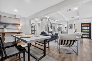 A modern living room with a dining area, a staircase, and a view of the outdoors. - Modern Stunner Walkable to Lake Travis + Views! (Austin)