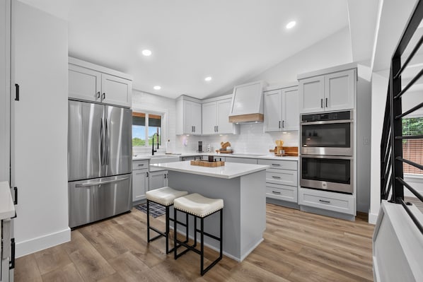 Una cocina moderna con electrodomésticos de acero inoxidable, armarios blancos y una isla central con taburetes.