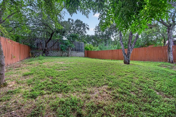 A backyard with a wooden fence, a stone wall, and a grassy lawn.