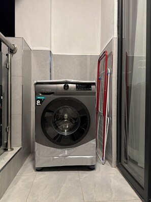 Een compacte, moderne wasmachine van Hisense in een hoek van een kamer met betegelde vloer en een glazen douchecabine.