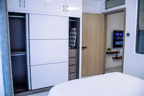 A bedroom with a bed, a wardrobe with multiple compartments, a door leading to a bathroom, and a mounted television. - Enjoy a stylish experience at this centrally-located 1-bedroom apartment (Nairobi)