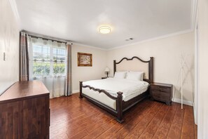A bedroom with a wooden bed, a nightstand, a dresser, and a window with curtains. - Beautiful 4-bedroom home, Comfortable, stylish and spacious (Baldwin Park)