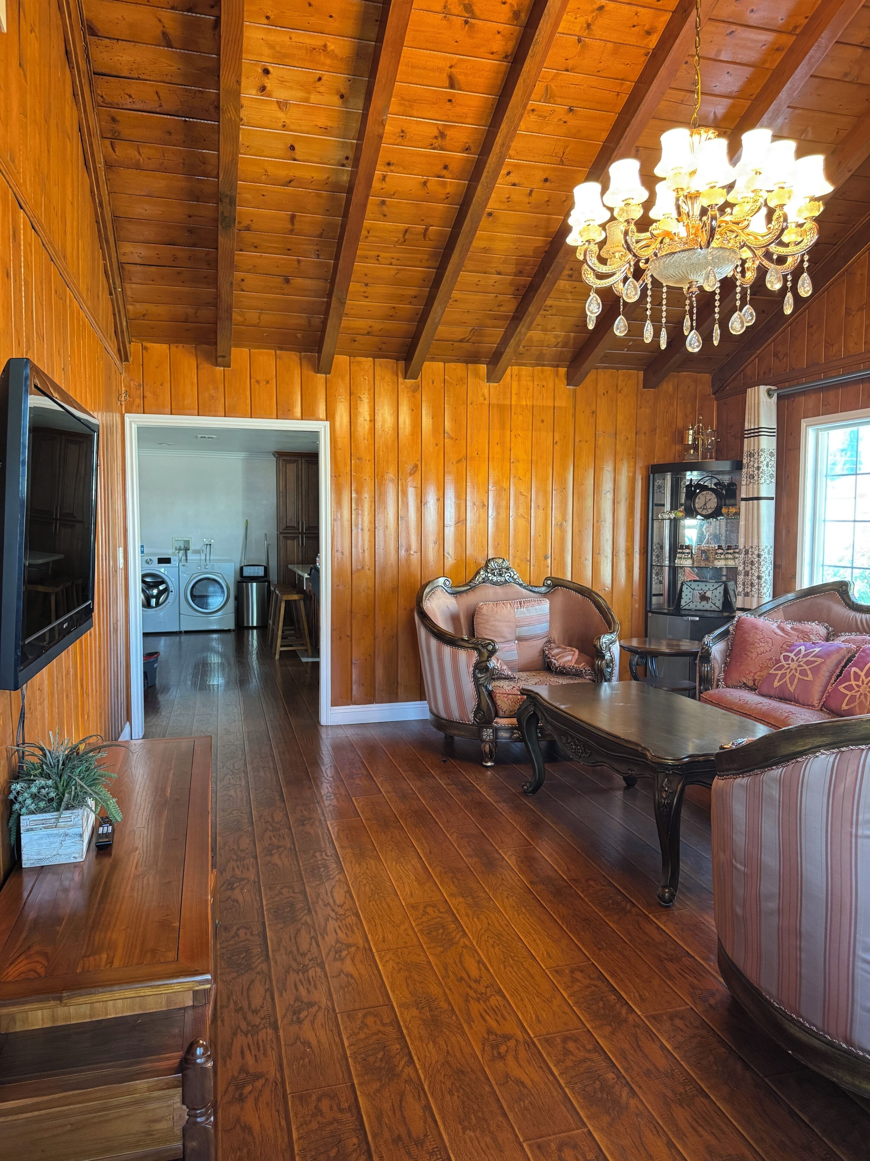 A wooden-paneled room with a chandelier, a sofa, a television, and a clock on the wall.