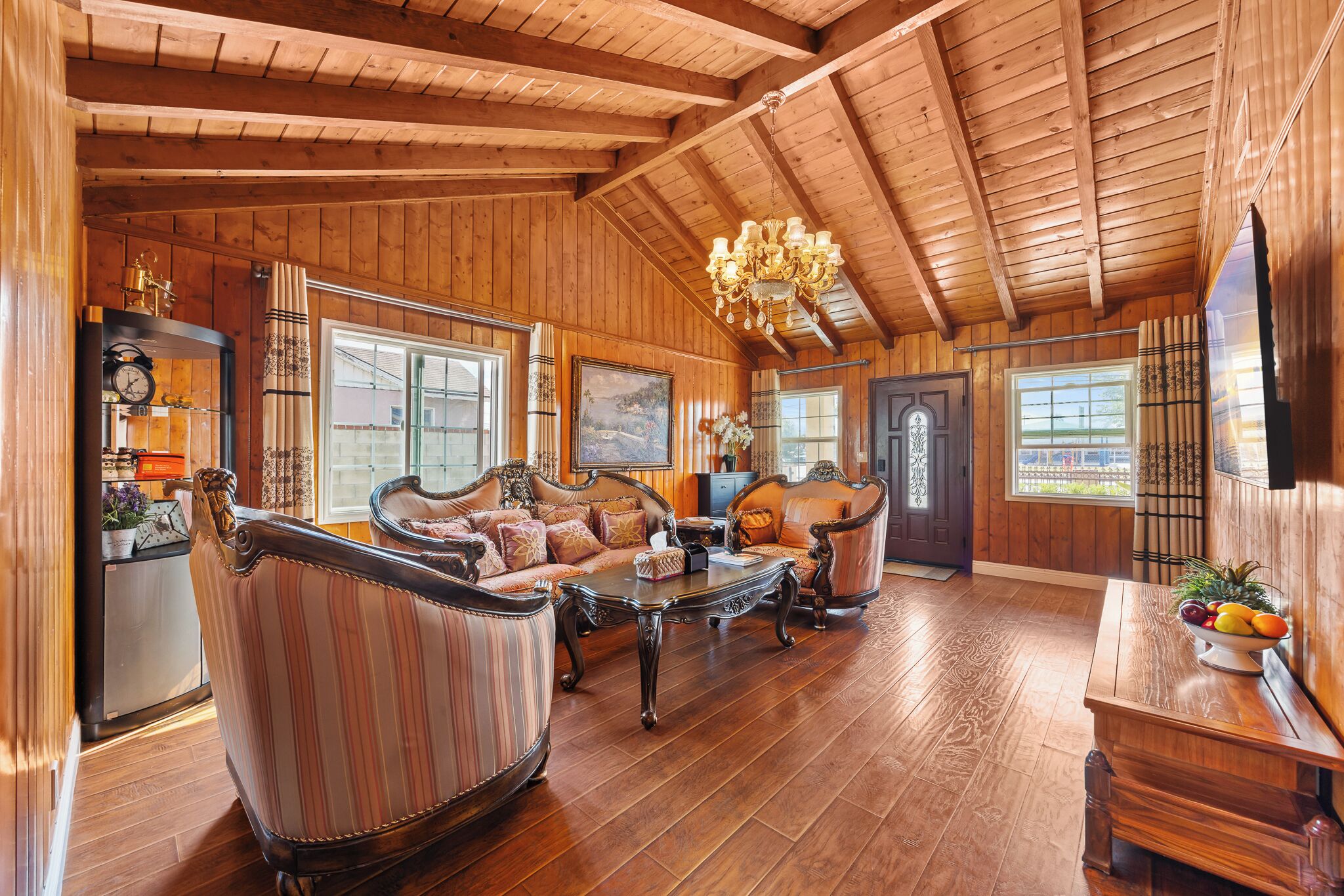 A spacious living room with wooden floors, a chandelier, and a large window.