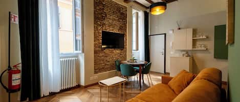 Una sala de estar moderna con un sofá, una mesa de comedor con sillas, una chimenea y un televisor montado en una pared de ladrillo.