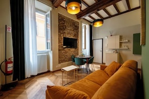 Ein modernes Wohnzimmer mit einer Couch, einem Esstisch mit Stühlen, einem Kamin und einem an einer Ziegelwand befestigten Fernseher.