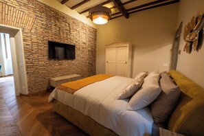 Ein Schlafzimmer mit Steinwand, einem Bett mit weißer Bettwäsche, Holzboden und einem an der Wand befestigten Flachbildfernseher.