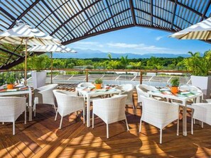 Un espace extérieur aménagé avec des meubles en osier blanc et des parasols, offrant une vue sur un paysage luxuriant.