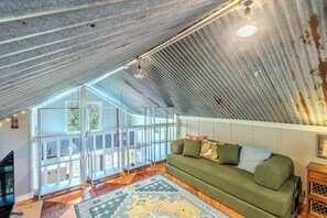 A loft-style room with a green sofa, patterned rug, and a view through large windows. - 10 min Walk to Downtown • Vintage Bungalow • Patio (McKinney)