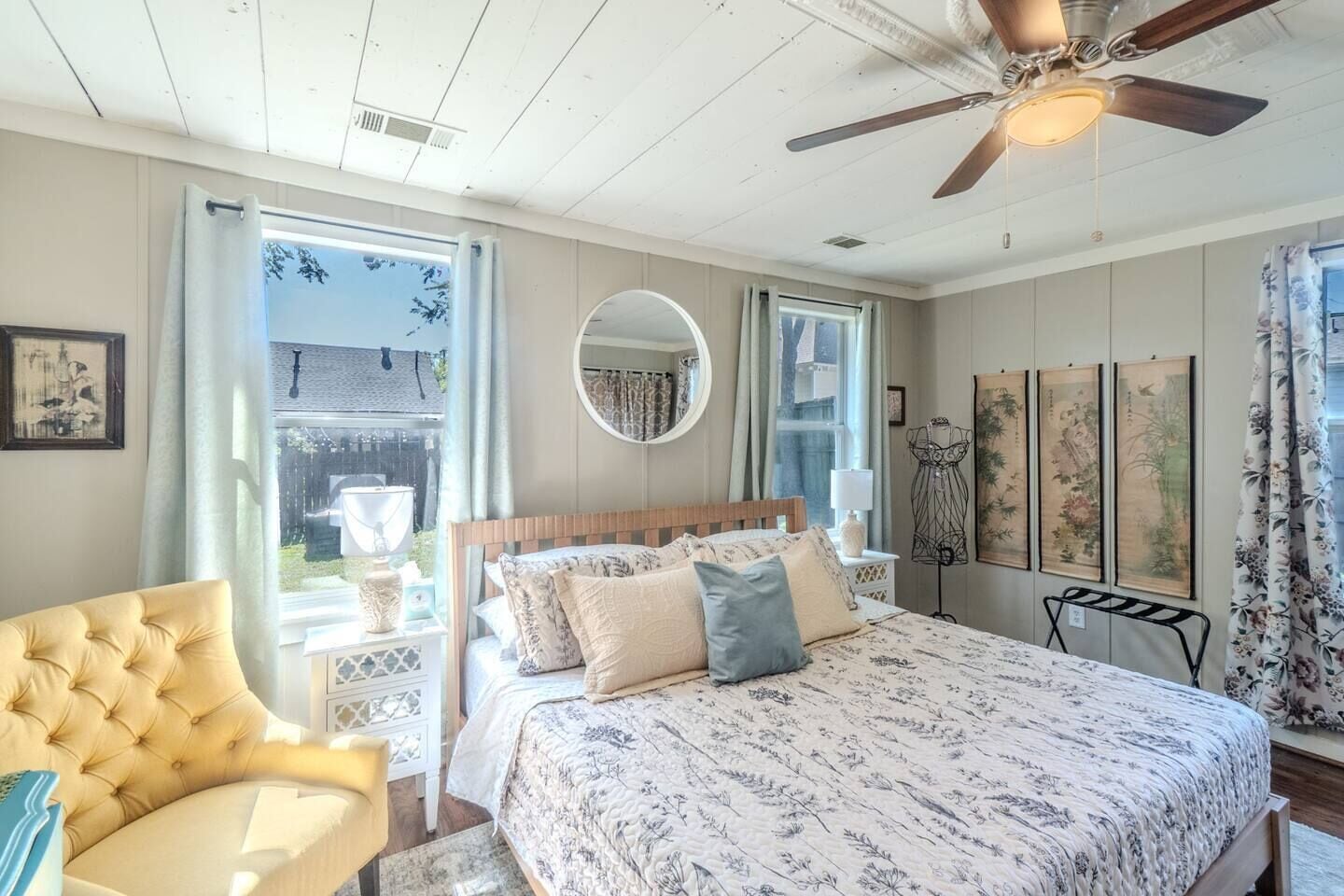A bedroom with a bed, a chair, a ceiling fan, and artwork on the walls.