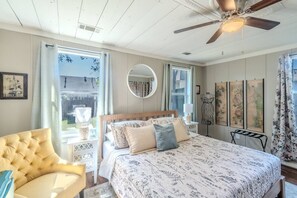 A bedroom with a bed, a chair, a ceiling fan, and artwork on the walls. - Patio • 10 min Walk to Downtown • Vintage Bungalow (McKinney)