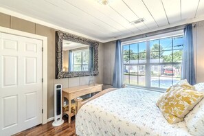 Une chambre à coucher avec un grand lit, une commode, un miroir et une fenêtre donnant sur l’extérieur.