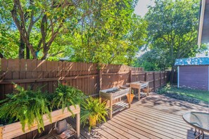 Eine Holzterrasse mit Tisch und Stühlen, umgeben von einem Holzzaun und viel Grün.