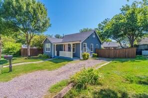 A single-story house with a porch, surrounded by a well-maintained lawn and a wooden fence. - 10 min Walk to Downtown • Vintage Bungalow • Patio (McKinney)