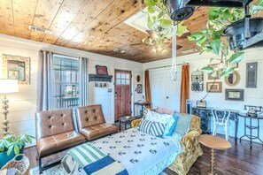 A cozy room with a wooden ceiling, a bed with patterned bedding, a brown leather sofa, and a dining area with a bar. - 10 min Walk to Downtown • Vintage Bungalow • Patio (McKinney)