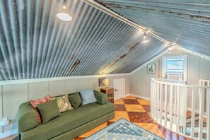 Ein Loft-Zimmer mit schrägverdeckter Decke, einem grünen Sofa, einem gemusterten Teppich und einer Treppe mit Geländer.