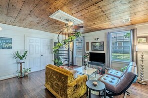 A living room with a wooden ceiling, a staircase, a TV, and a fireplace. - Patio • 10 min Walk to Downtown • Vintage Bungalow (McKinney)
