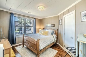 Ein Schlafzimmer mit einem Holzbett, einem fenster mit Vorhängen, einer Nachttischlampe und einer Tür.