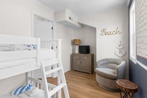 A child's bunk bed, a television on a cabinet, a chair, and a wall with the word 'Beach' and an anchor decoration. - Beach Please, Ocean Front Retreat (Ocean Isle Beach)