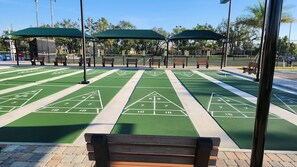 Un terrain de jeu de shuffleboard doté d’une surface verte et de marquages blancs, entouré de bancs et de zones abritées.
