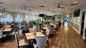 A restaurant with multiple tables and chairs, a bar area, and a television screen.
