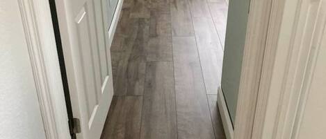 A hallway with wooden flooring, white doors, and a window with blinds.