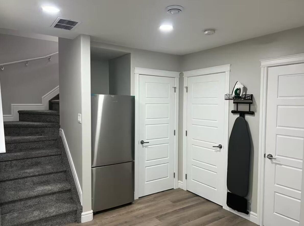 A hallway with a refrigerator, double doors, and a staircase.