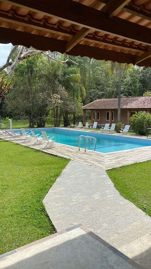 Ein Swimmingpool mit Liegestühlen, eine überdachte Terrasse und ein Backsteinhaus im Hintergrund.