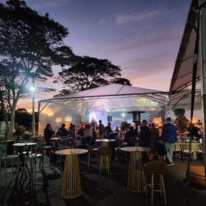 An outdoor dining area with round tables and chairs, under a large transparent tent.