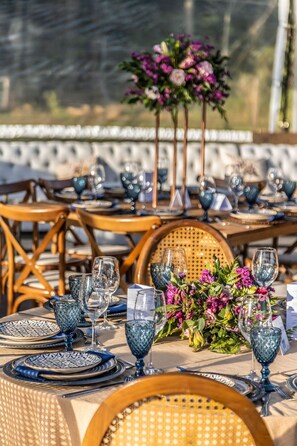 A table set with blue glassware and plates, a floral centerpiece, and wicker chairs.