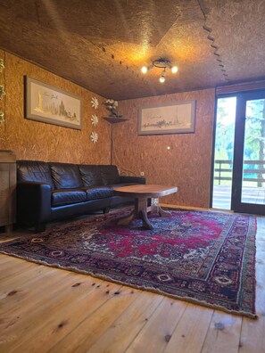 A cozy living room with a wooden ceiling, a black leather sofa, a wooden coffee table, and a patterned rug. - Mountain Retreat Maslo (Babino Polje)