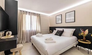 A modern hotel room with a large bed, a flat-screen TV, a bedside table with a lamp, and a window with sheer curtains. - TASTEFULLY DECORATED WITH MODERN ELEGANCE, STEPS FROM LA CROISETTE & BEACHES. (Cannes)