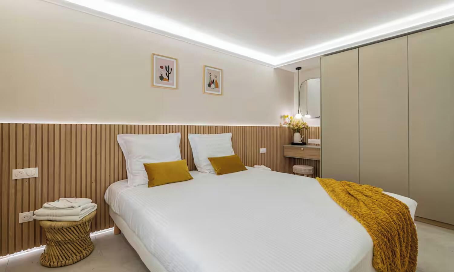 A modern bedroom with a large bed, bedside tables, a wardrobe, and two wall-mounted artworks.