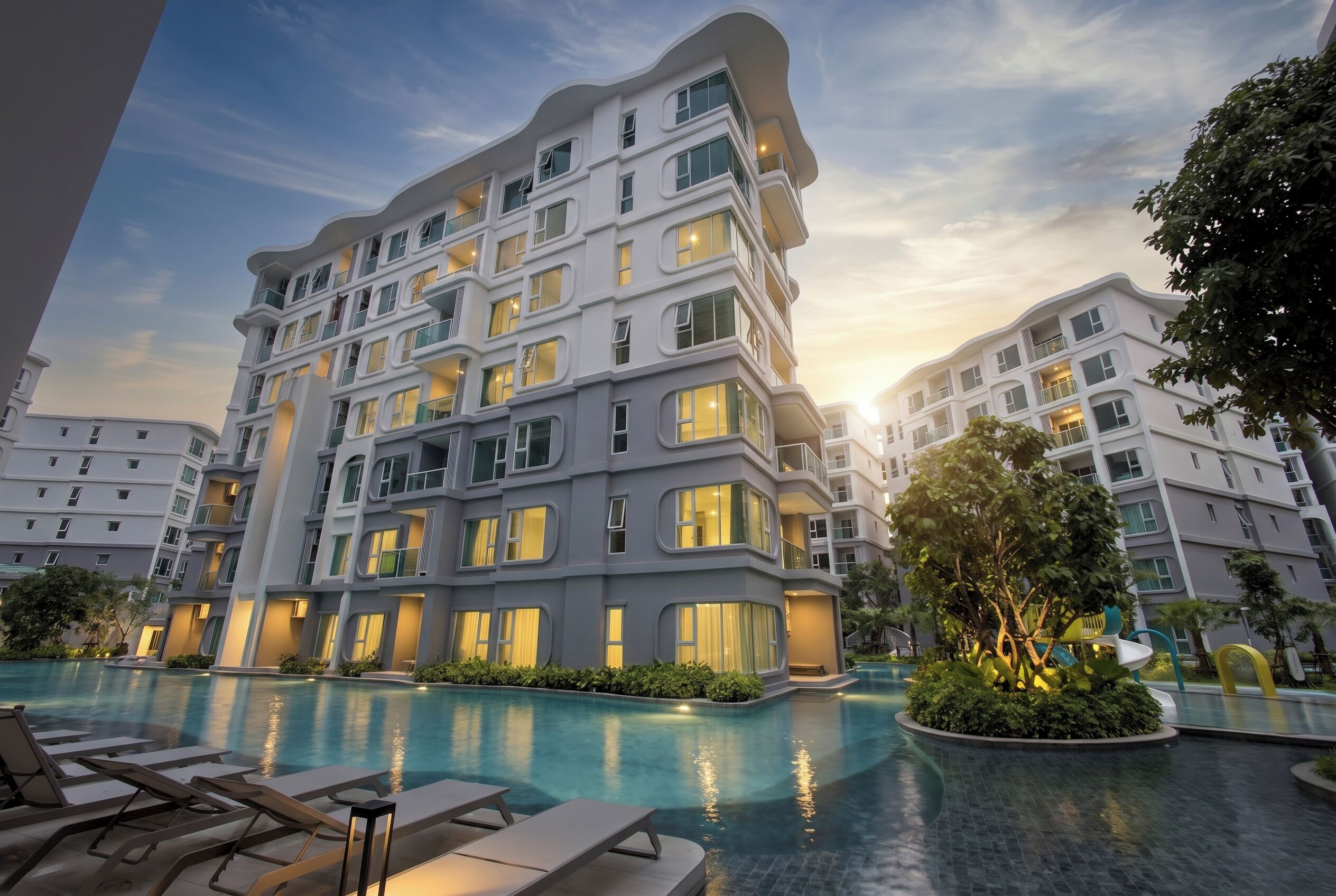 A multi-story hotel with a swimming pool, outdoor seating, and lush landscaping.