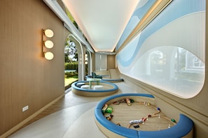Ein modernes Interieur mit einer gebogenen Sitzgruppe, einem Kinderspielbereich und großen Fenstern mit Blick ins Freie.